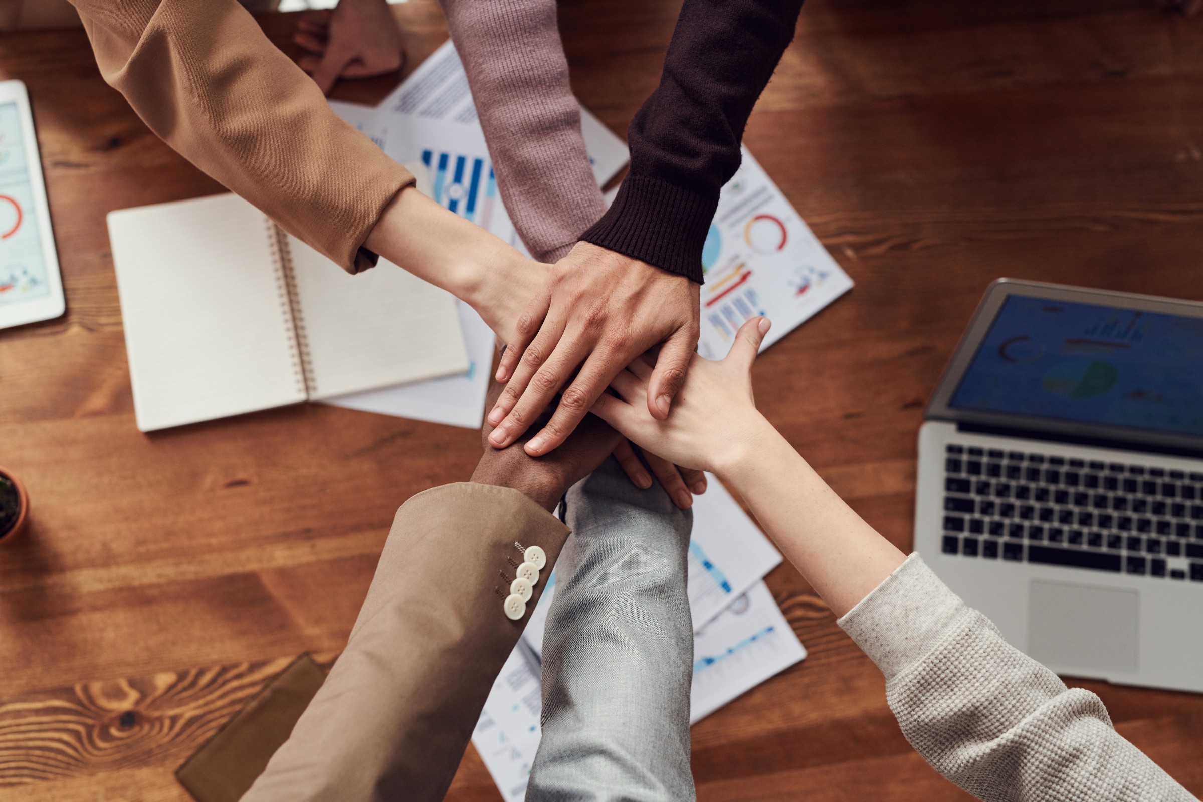 Six people's arms extended with hands meeting in the center.
