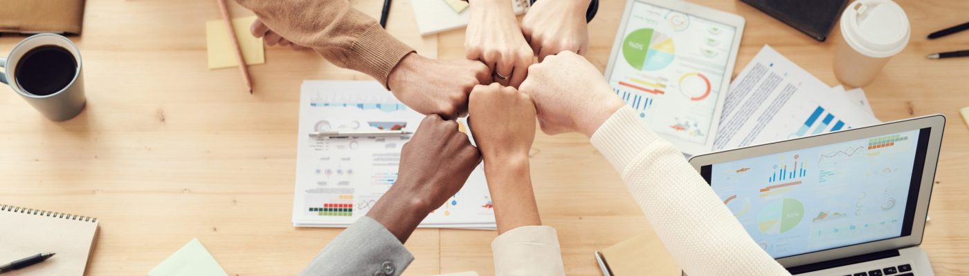 people reaching their arms across a desk and putting their fists together