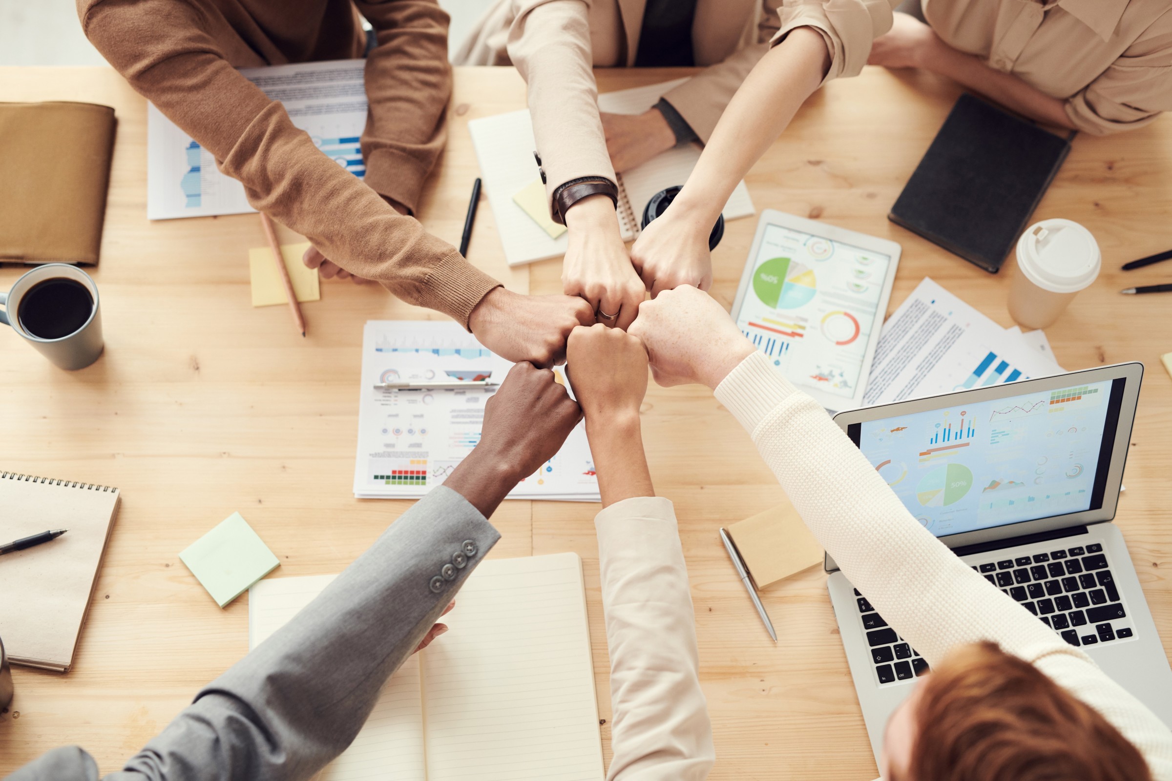 people reaching their arms across a desk and putting their fists together