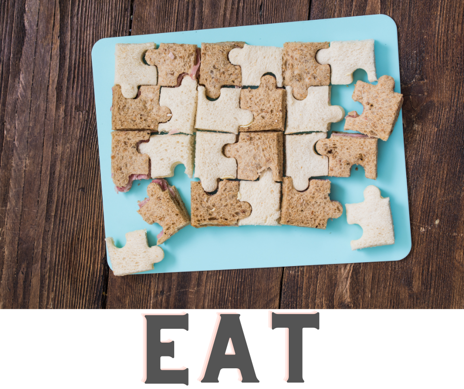 Tray of sandwiches cut into puzzle pieces with the word EAT at the bottom.