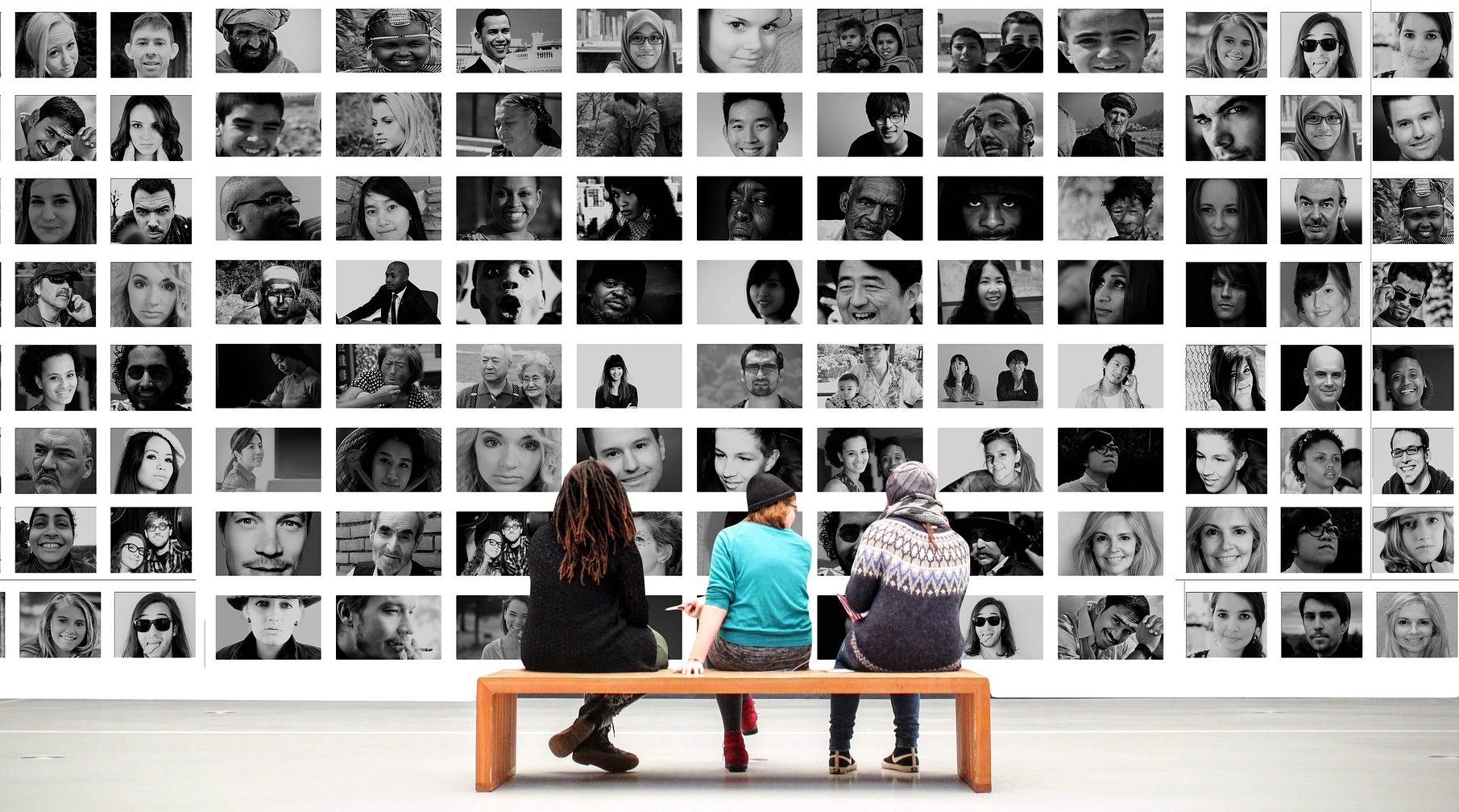 Three individuals siting on a bench looking at a gallery of black and white portraits.
