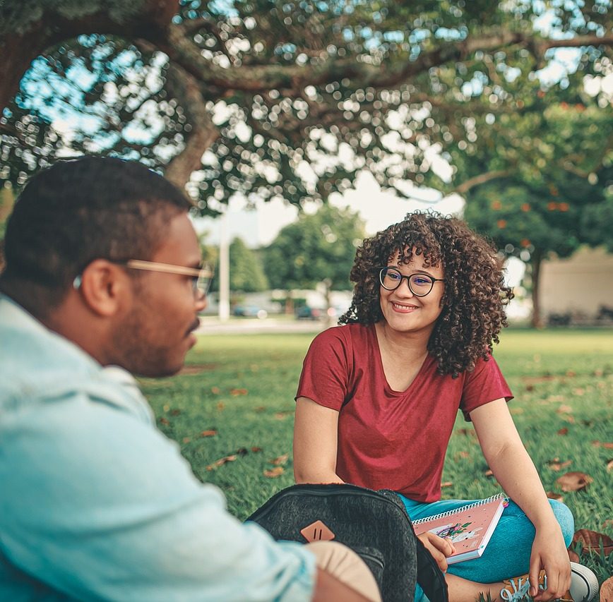 Individuals sitting in the grass in a park talking.