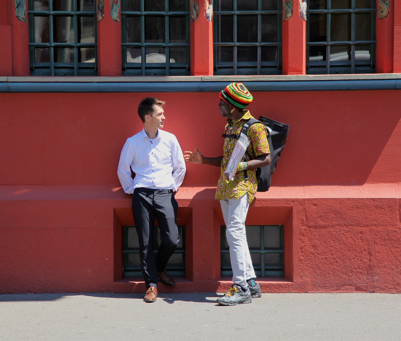 Two individuals from different backgrounds standing outside a building talking.